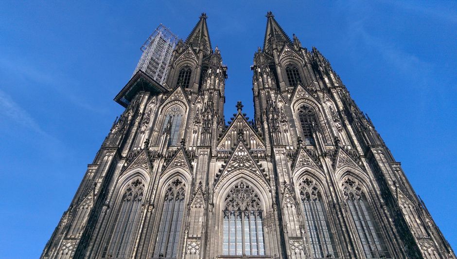 A low angle view of Cologne Cathedral's gothic architecture against a clear blue sky.