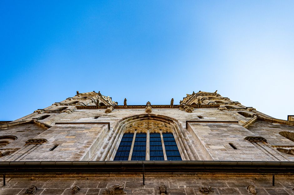 Upward view of a Gothic cathedral under clear blue sky, featuring intricate architecture.